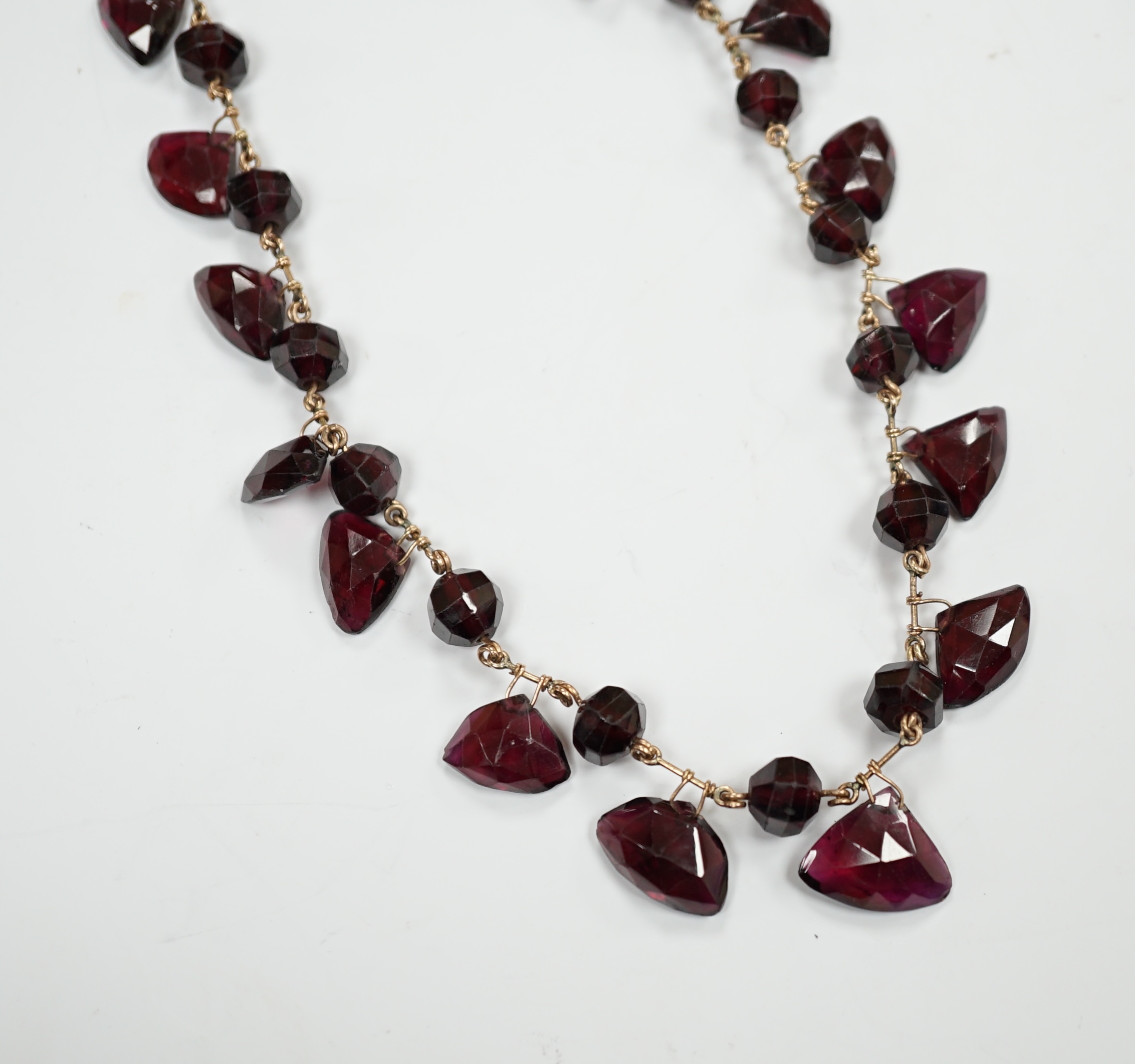 A Victorian yellow metal (test as 9ct) and garnet drop fringe necklace, set with faceted circular and pebble cut stones, 38cm, gross weight 32.6 grams.